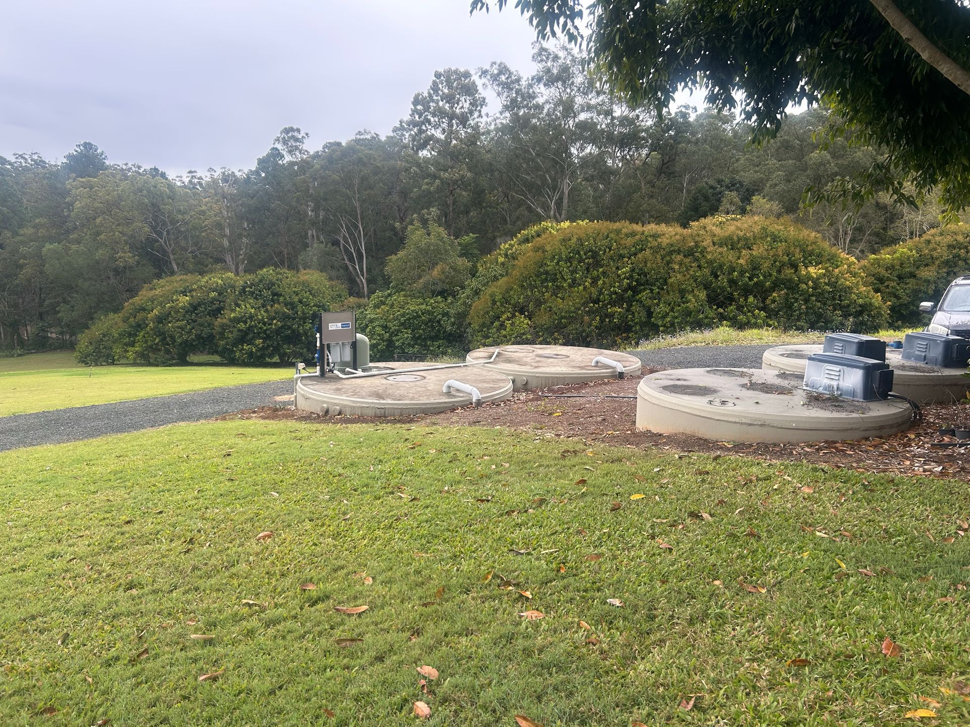 Grassy backyard with a small concrete patio, outdoor equipment, and trees in the background