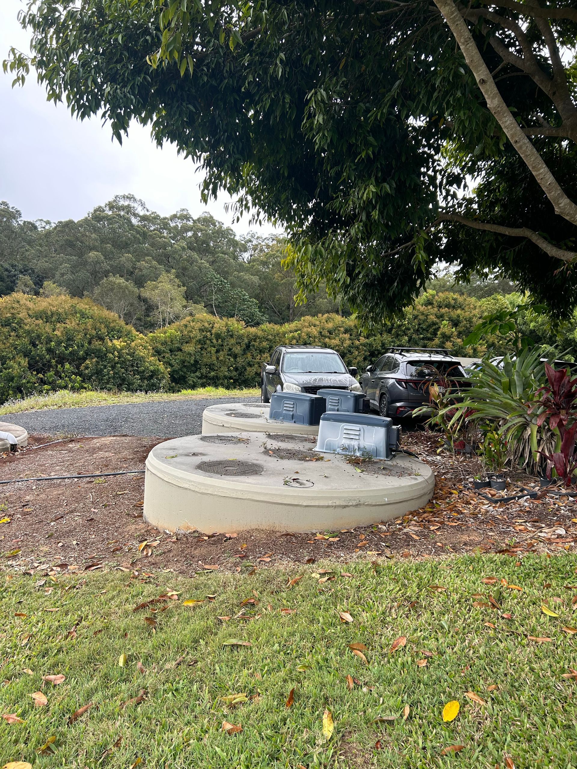 Outdoor motor on circular concrete base in a grassy park, surrounded by trees and shrubs.