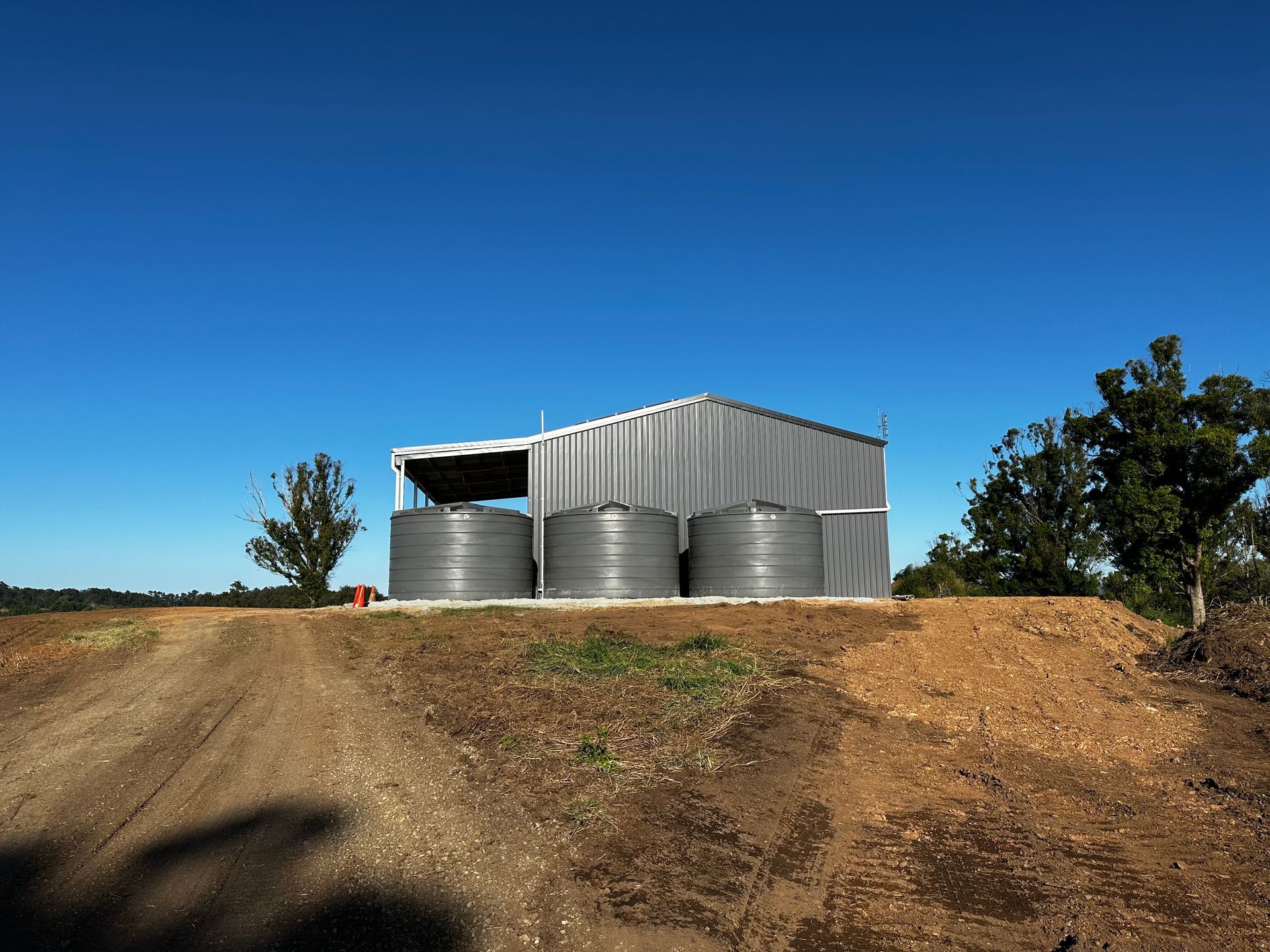 Metal water tanks beside a corrugated shed on a dirt hill under a clear blue sky