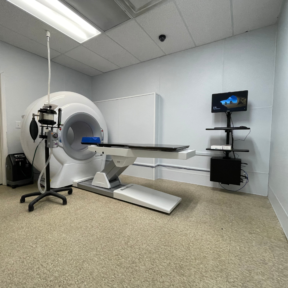 Medical exam room with a white PET scanner, table, and monitor.