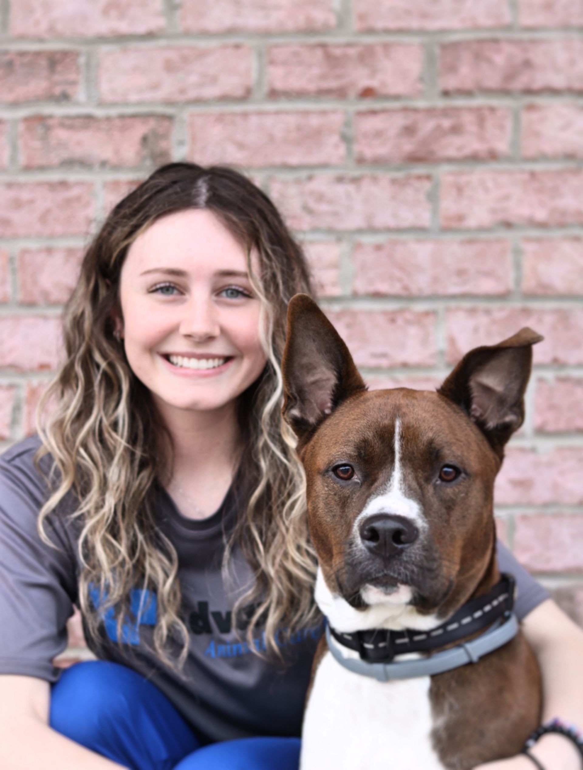 Woman smiling with a brown and white dog in front of a brick wall.