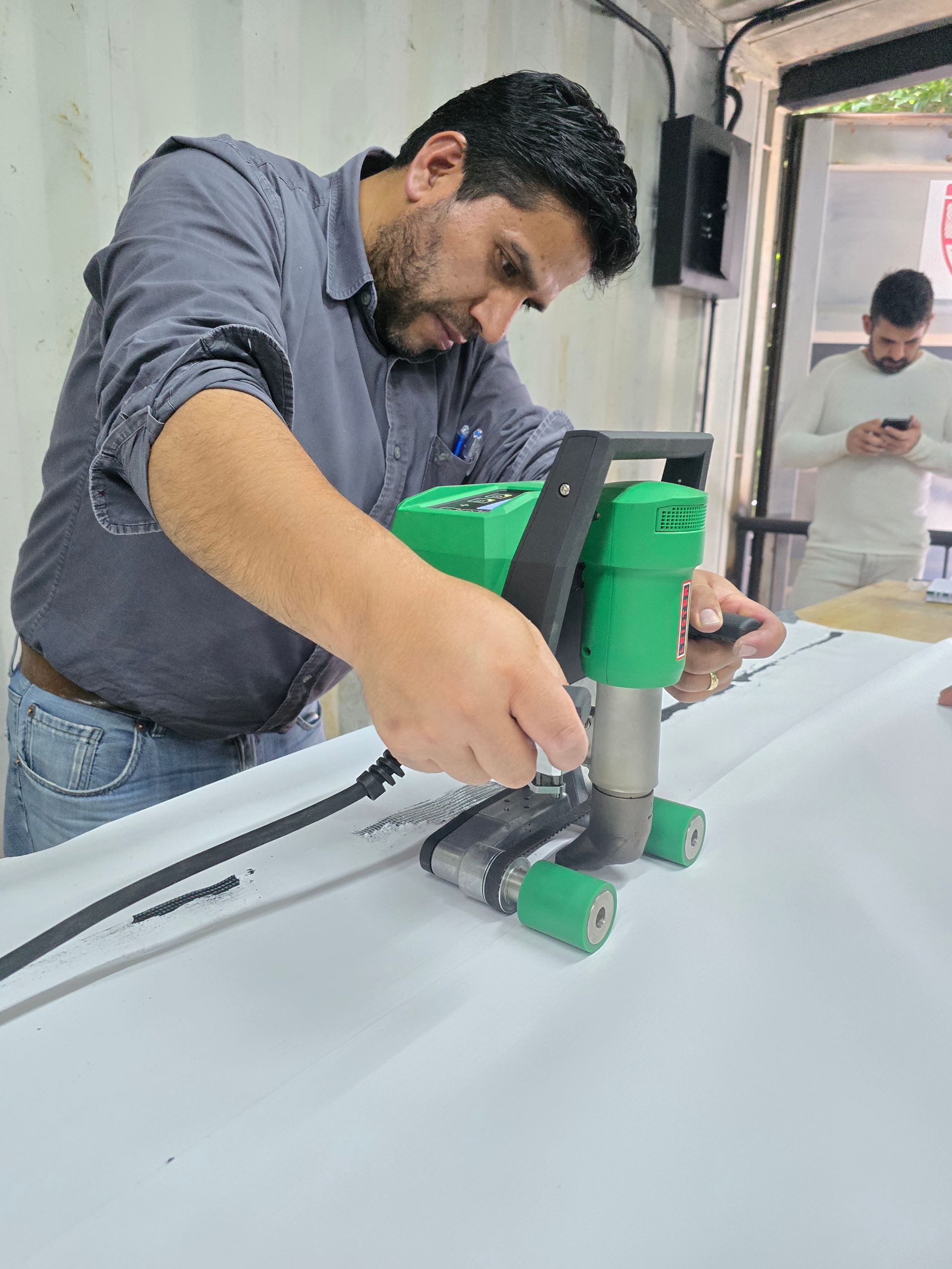 Hombre utilizando una herramienta manual verde para cortar material blanco en un banco de trabajo en un taller.