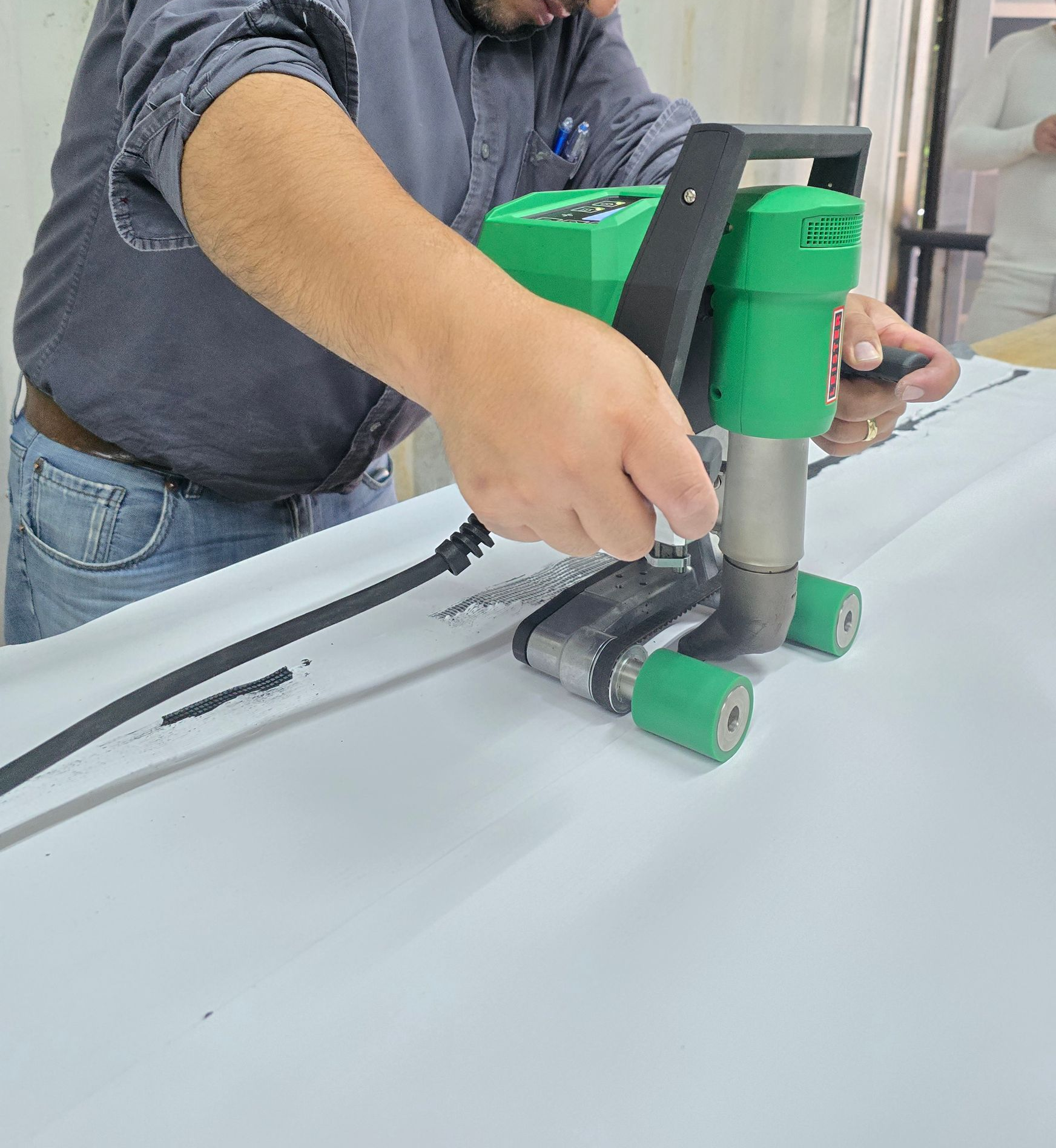 Persona utilizando una herramienta manual verde sobre una superficie blanca en un taller.