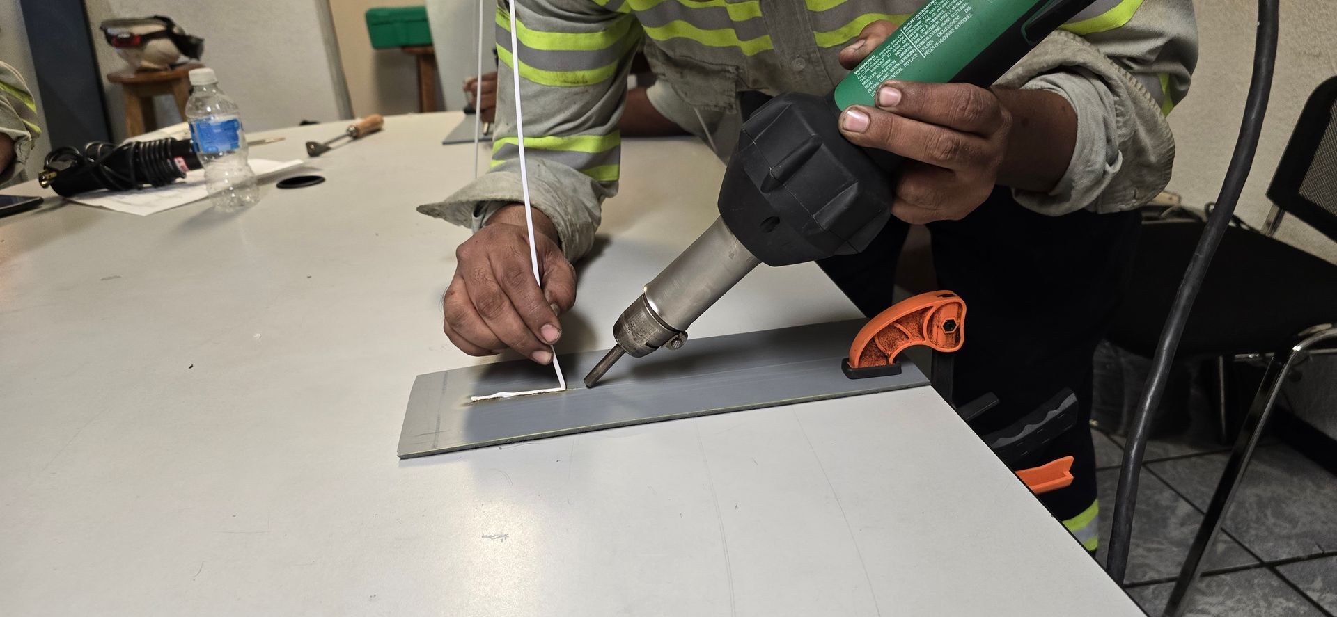 Un trabajador aplica adhesivo con una pistola de calafateo sobre una mesa en un taller.