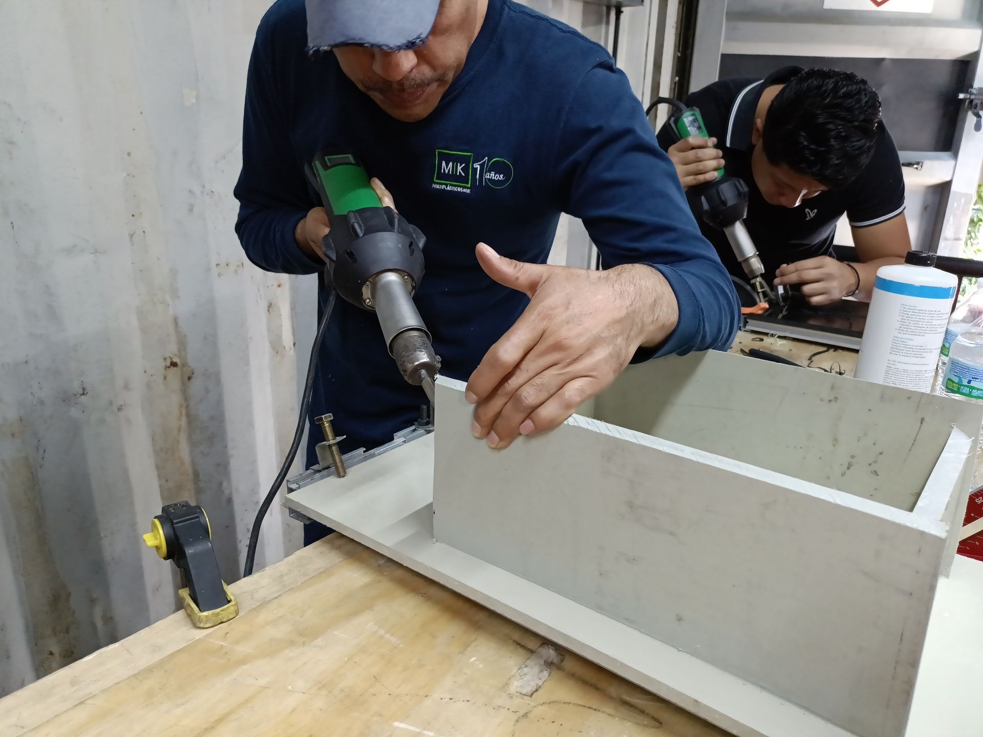 Dos trabajadores ensamblan un armario blanco con un taladro eléctrico en un taller.