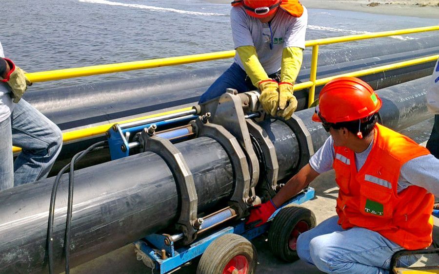 Unos trabajadores con cascos naranjas reparan un gran oleoducto en la cubierta de un barco.