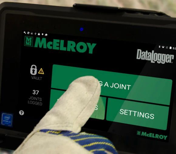 Pantalla verde del registrador de datos McElroy pulsada con un dedo enguantado y botones de configuración conjunta