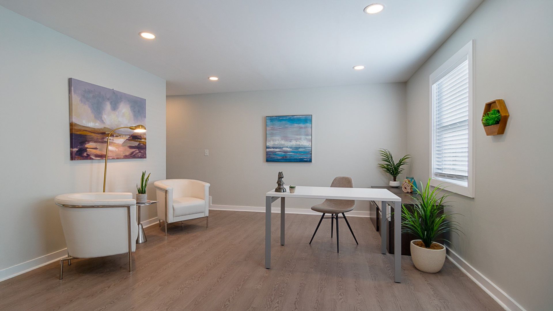 Bright minimalist dining room with white table, chairs, plants, and wall art in a neutral-toned home