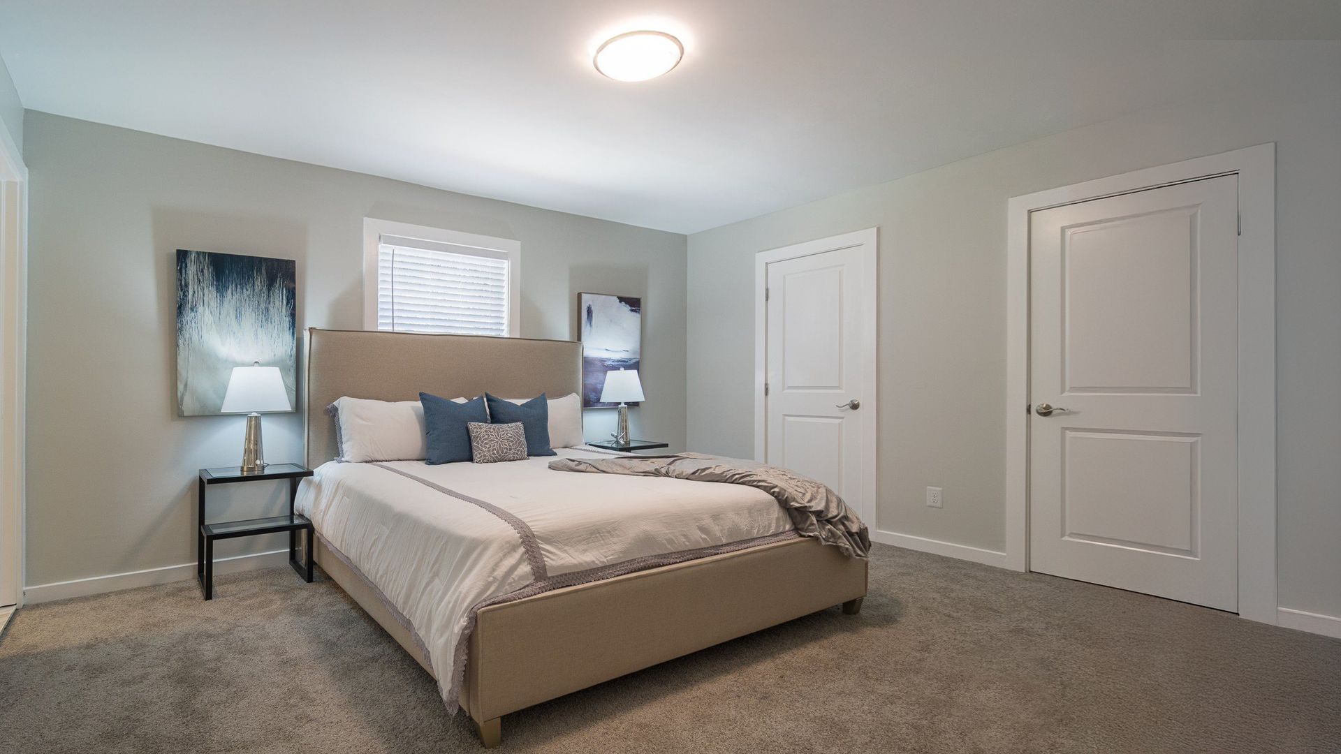 Modern bedroom with a neatly made bed, gray carpet, and white doors and walls