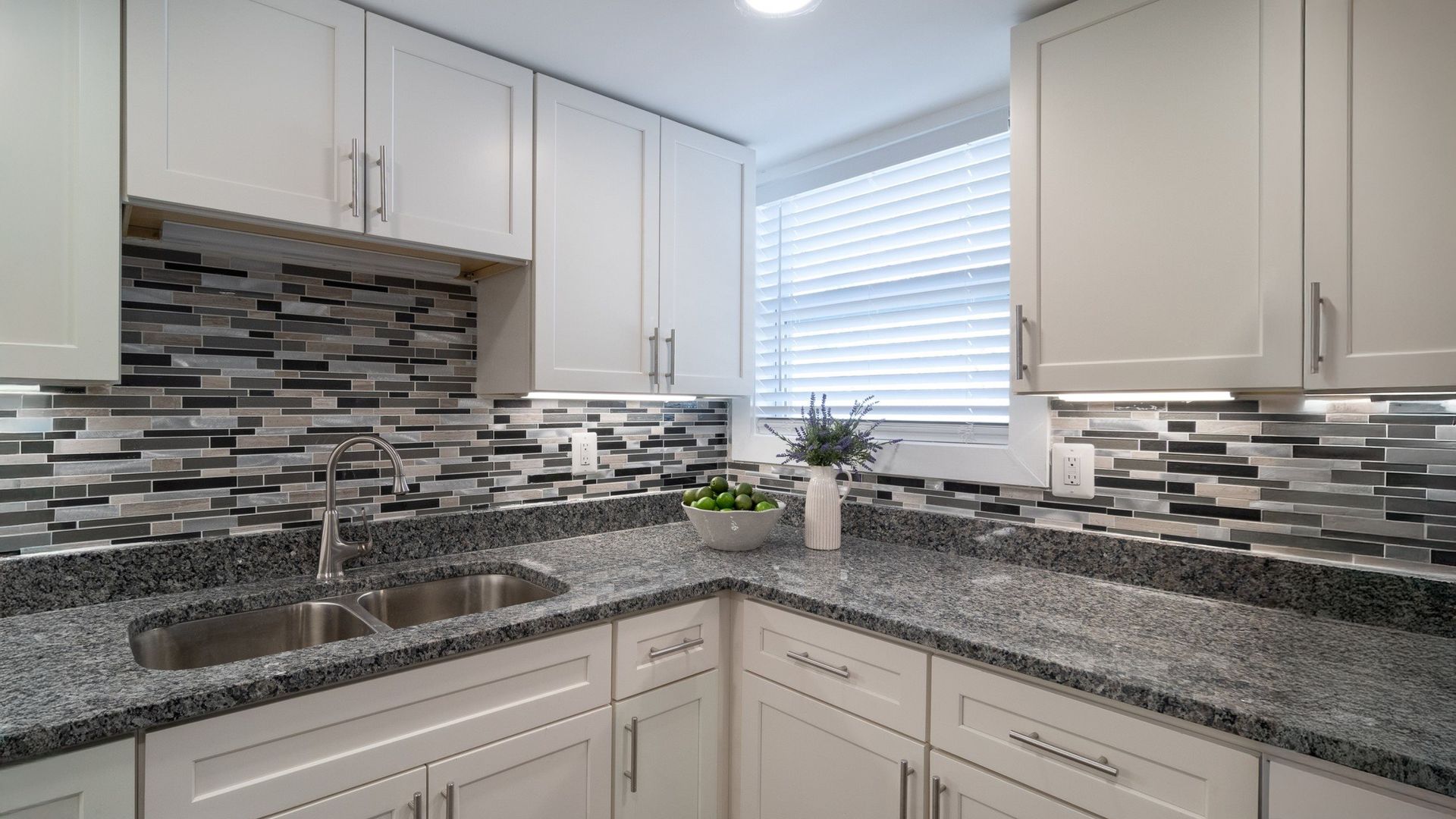 Bright modern kitchen with white cabinets, gray tile backsplash, and granite countertops by a window