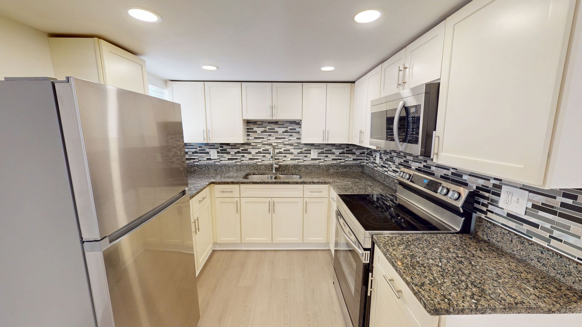 Bright modern kitchen with white cabinets, gray granite counters, and mosaic tile backsplash by a window