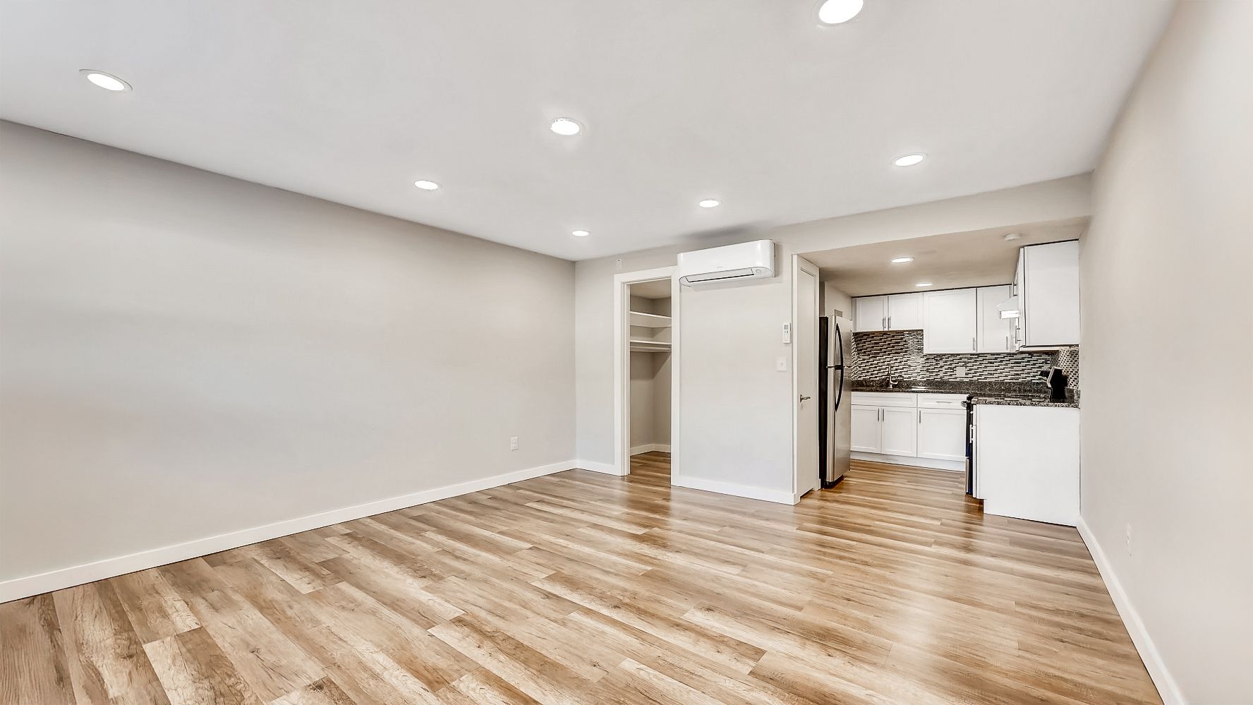 Empty modern room with light wood floors, recessed lights, and open closet/storage area