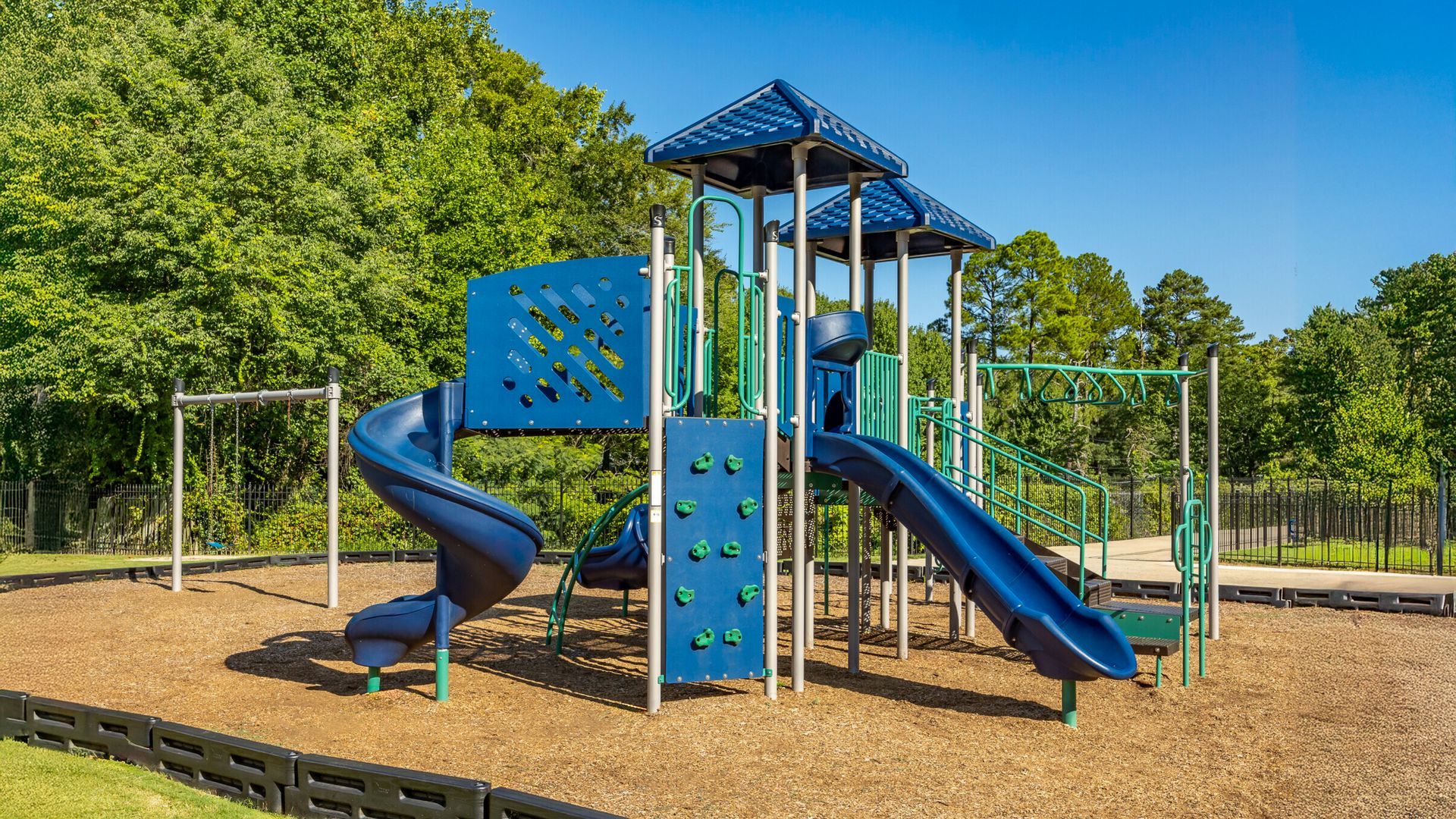 Blue playground climbing structure with slides and swings in a sunny park