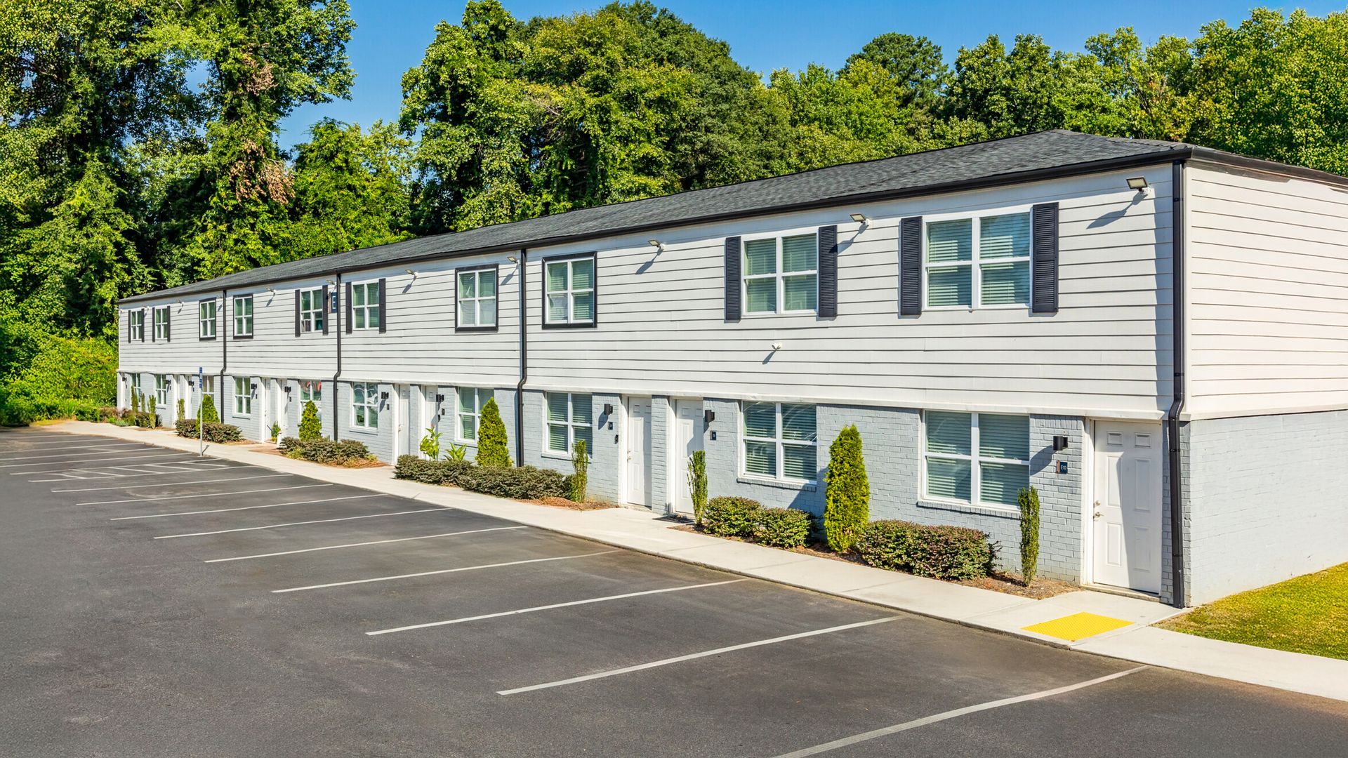 Long white two-story motel with rows of doors and windows beside an empty parking lot and trees