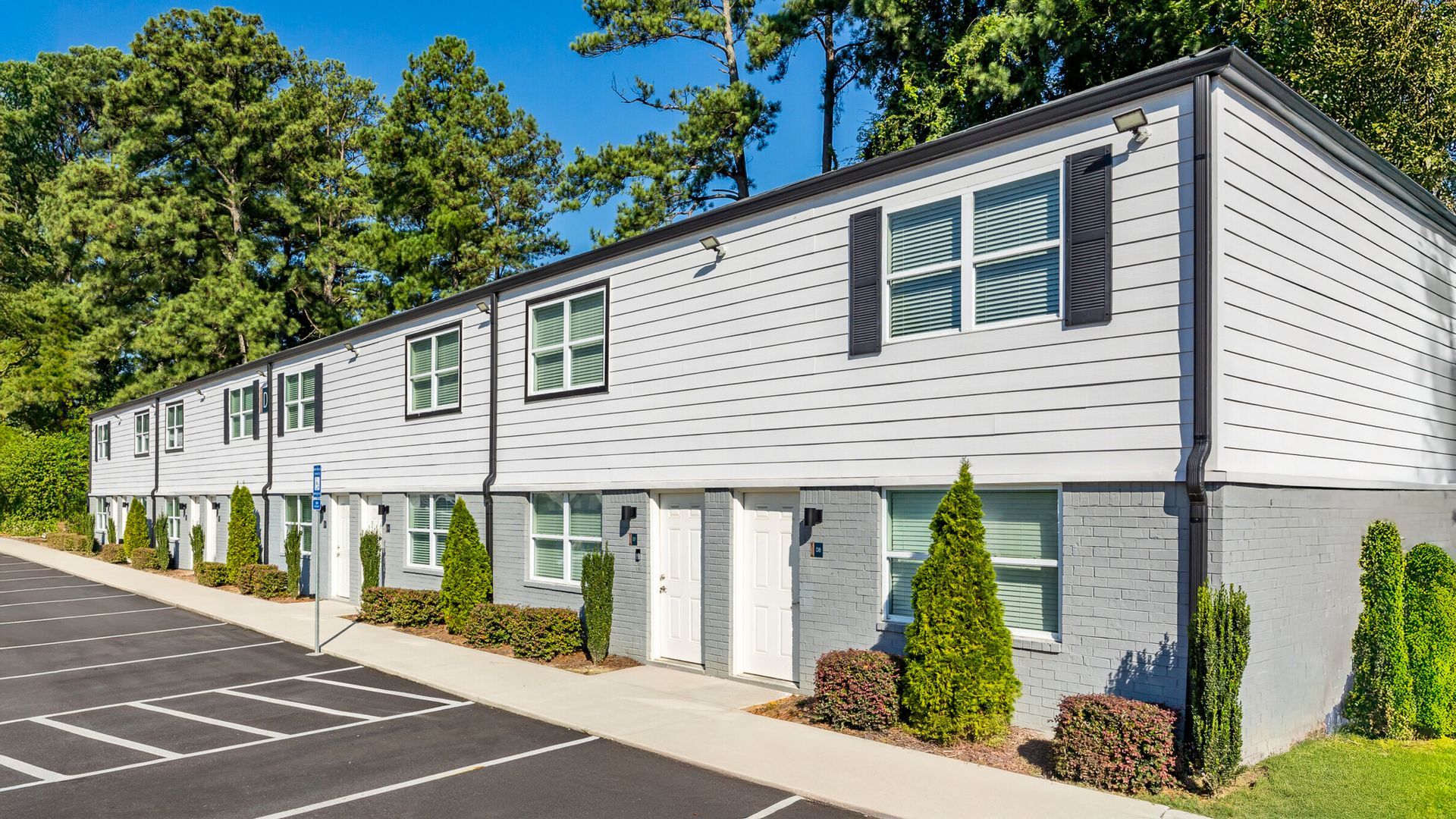 Row of white two-story townhouses beside an empty parking lot under bright sunlight
