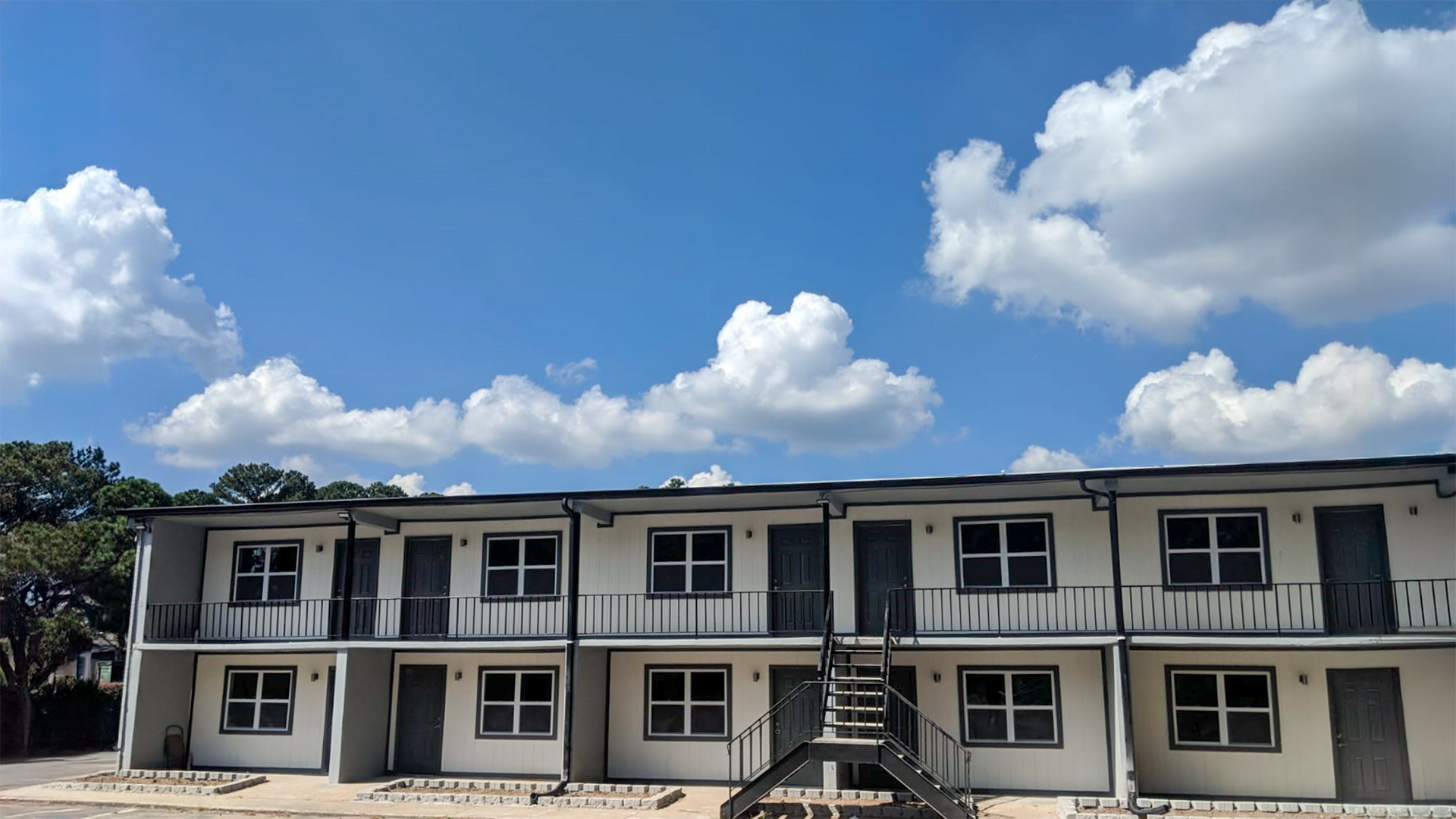 Two-story beige apartment building under a bright blue sky with large white clouds