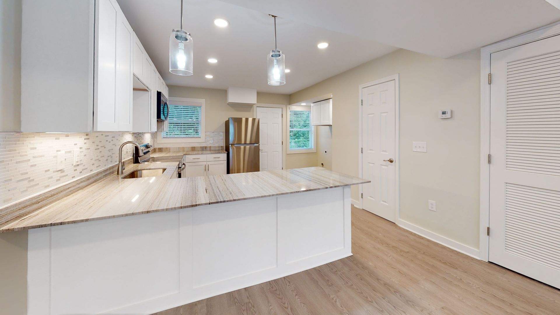 Bright modern kitchen with white cabinets, large island, stainless appliances, and wood floors