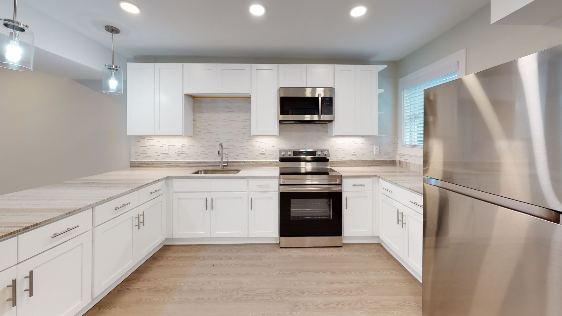 Bright modern white kitchen with stainless steel appliances, tiled backsplash, and large window.