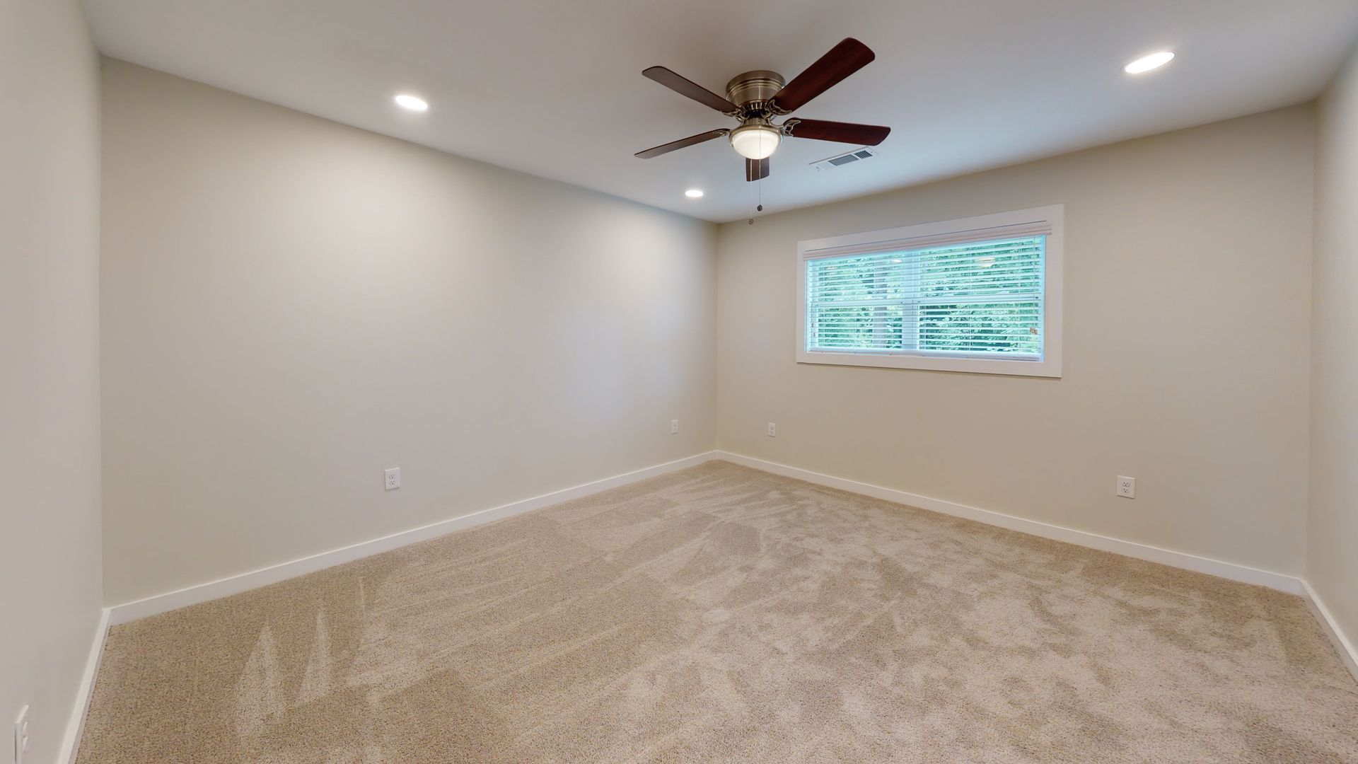 Empty beige bedroom with carpet, ceiling fan, and a window letting in natural light