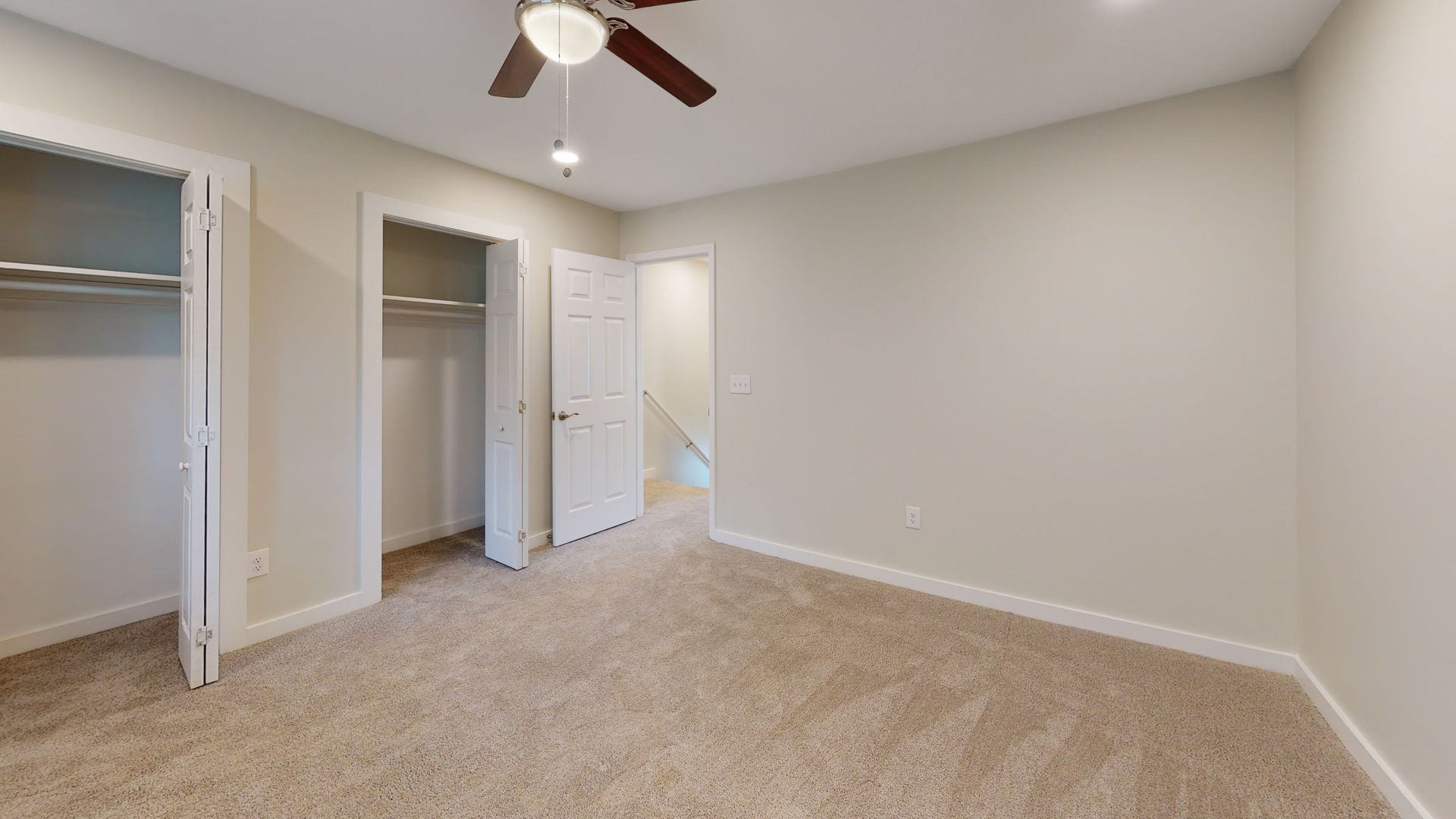Empty beige bedroom with carpet, open closet, and ceiling fan on a white ceiling.
