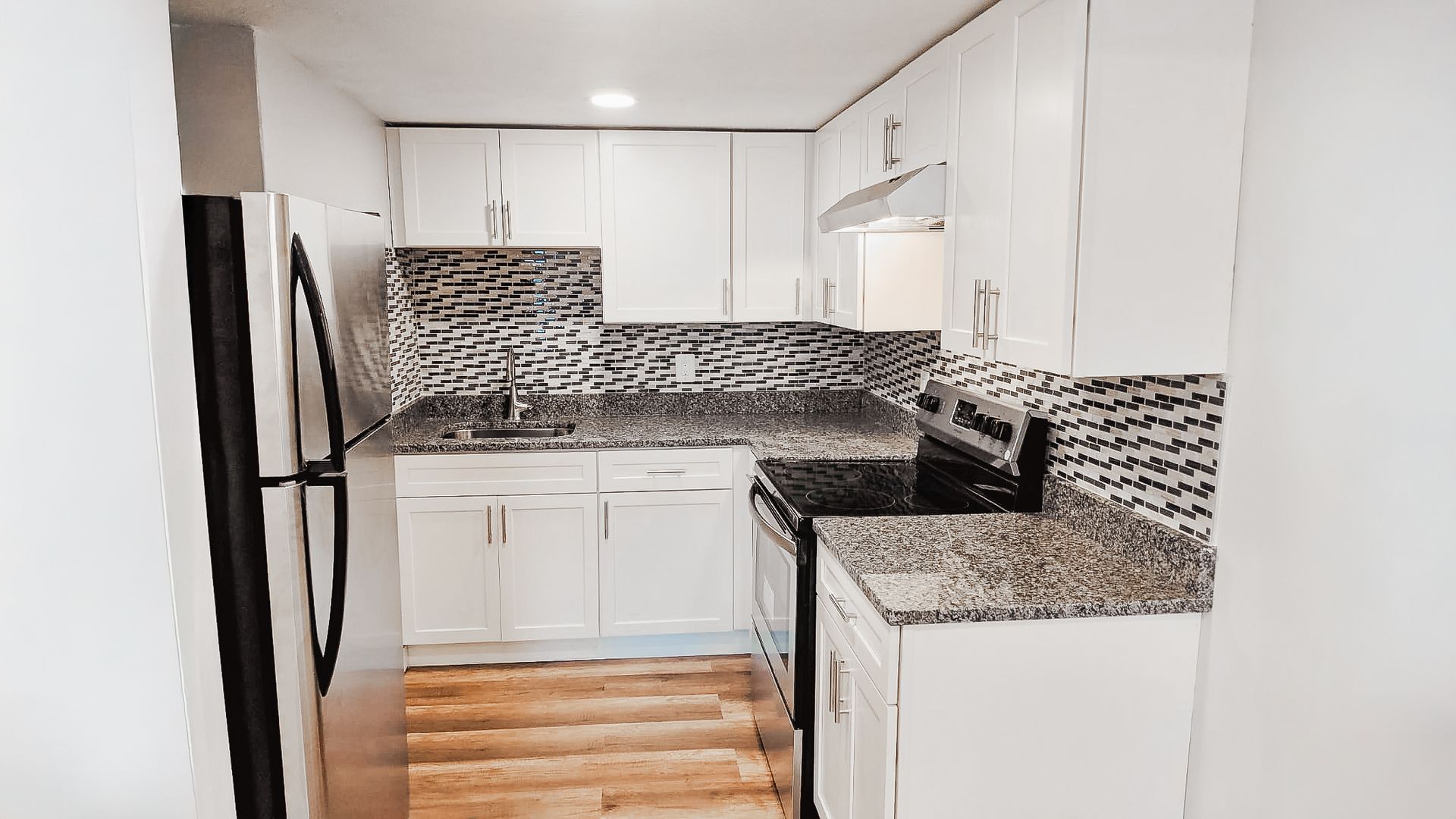 Modern white kitchen with black-and-white backsplash, granite counters, and stainless-steel refrigerator