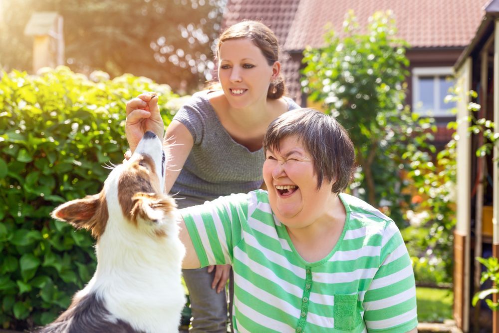 Woman With a Disability Smiles While the Other Woman Feeds a Treat — Canine Training School in Trinity Park, QLD