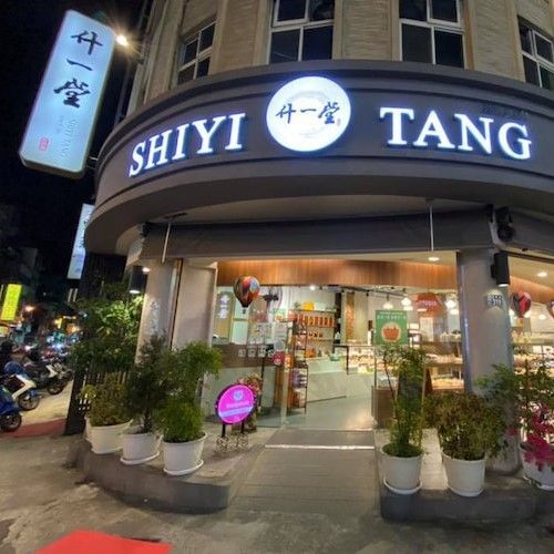 夜幕降臨，石一堂店面招牌明亮醒目，玻璃門面敞開，店外擺放著盆栽植物。
