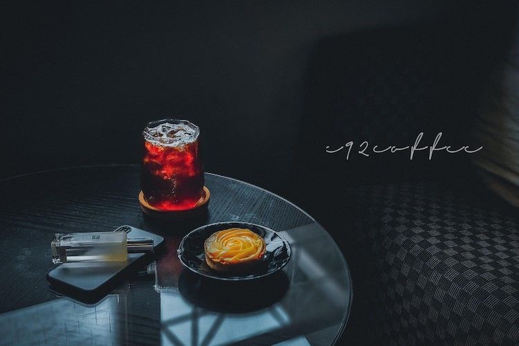 小桌上的咖啡：一杯紅色的飲料、一塊糕點和一本筆記本，置身於昏暗的咖啡館環境中。