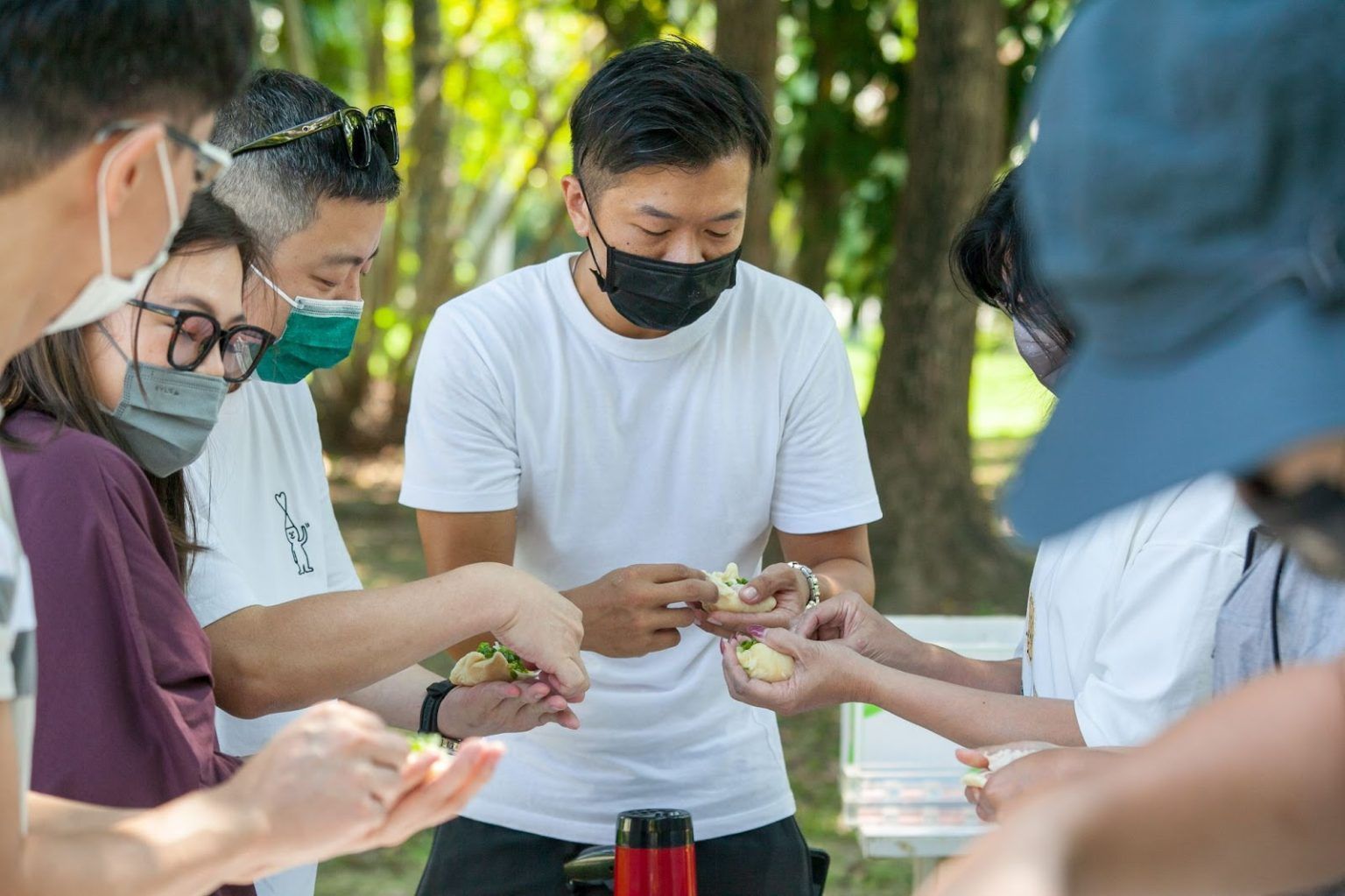 一群戴著口罩的人在公園的戶外桌旁分享食物