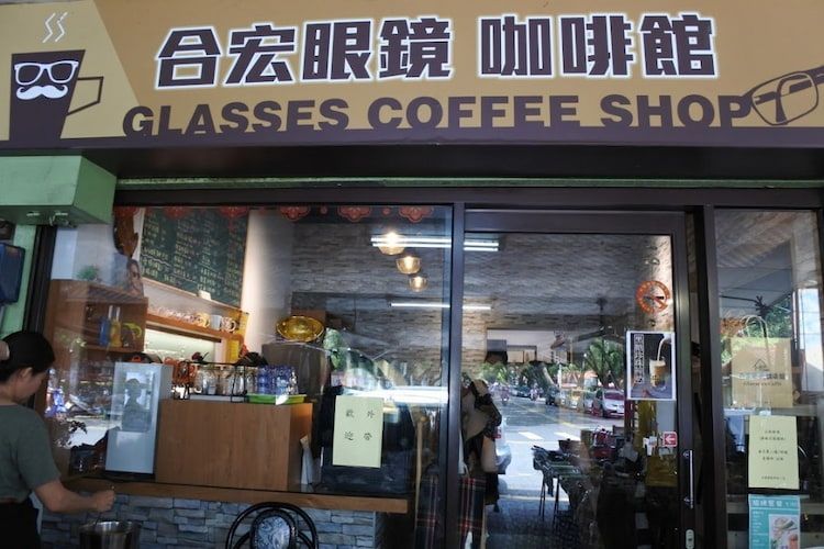 玻璃咖啡店的店面，黃色招牌寫著​​中英文，門口站著一個人。