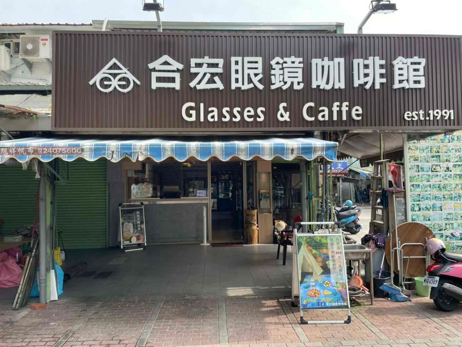 棕色遮陽篷上掛著「眼鏡和咖啡」的店面招牌，還有一個小小的咖啡館入口和戶外展示架。