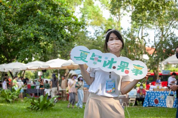 一名女子在公園的戶外活動中舉著一塊寫有綠色和橘色中文的牌子。