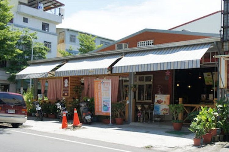 在陽光明媚的日子裡，街邊咖啡館的條紋遮陽篷、盆栽植物和停放的汽車構成了美麗的景象。