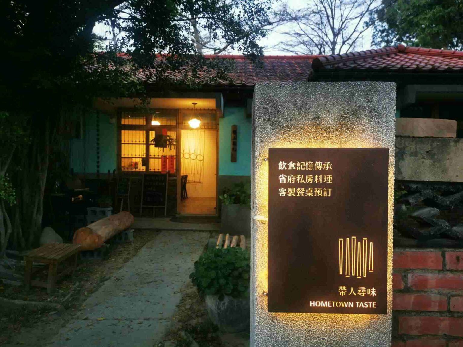 黃昏時分，燈光溫暖的咖啡館外景，閃亮的招牌和通往入口的花園小徑。