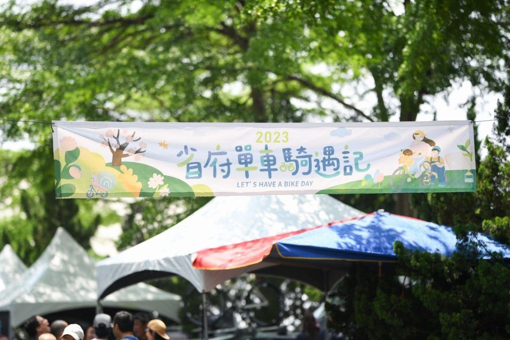 綠樹下,五彩繽紛的帳篷上方懸掛著印有中文的戶外節慶橫幅。