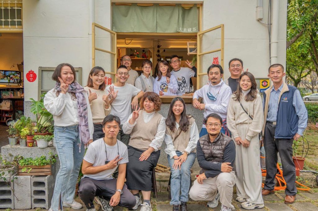 一群人在建築物入口外擺姿勢拍照，面帶微笑，揮手致意。