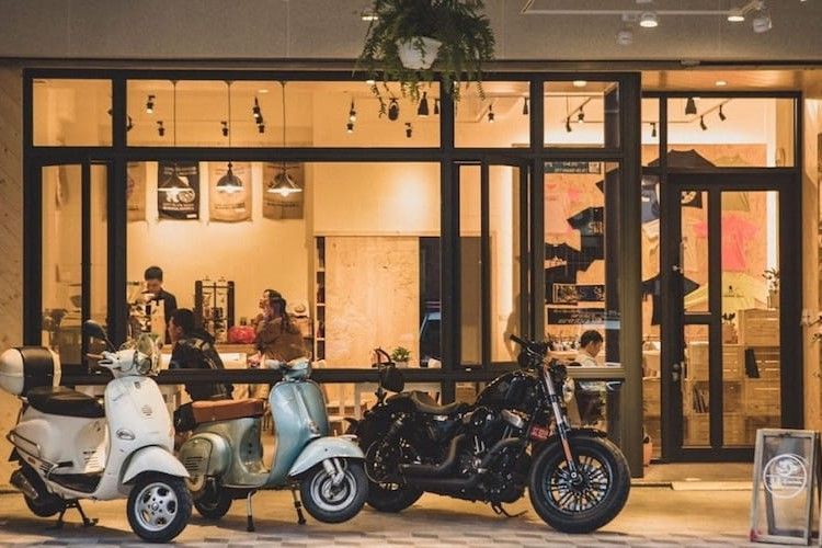 夜裡，幾輛踏板車和一輛黑色摩托車停在一家燈光溫暖的咖啡館外。
