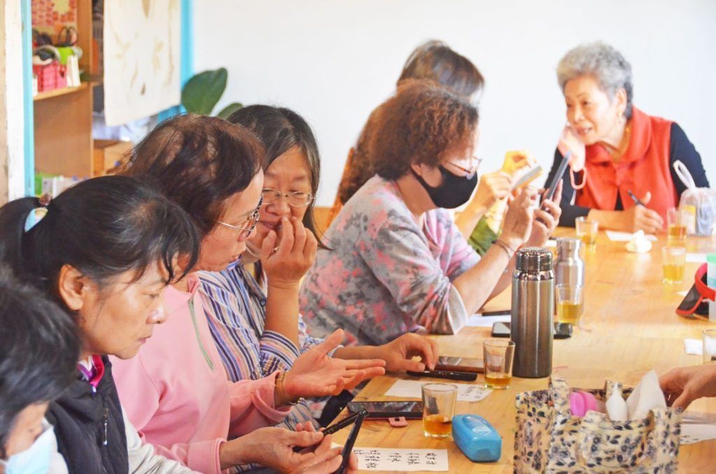 在一家明亮的咖啡館裡,人們坐在桌旁,一邊聊天一邊使用智慧型手機。