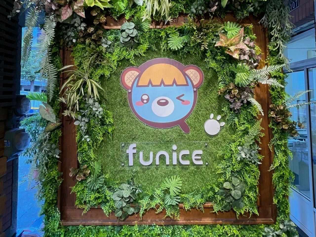在綠葉繁茂的牆面上印有 Funice 的標誌，旁邊還有一個藍粉色的卡通熊臉。