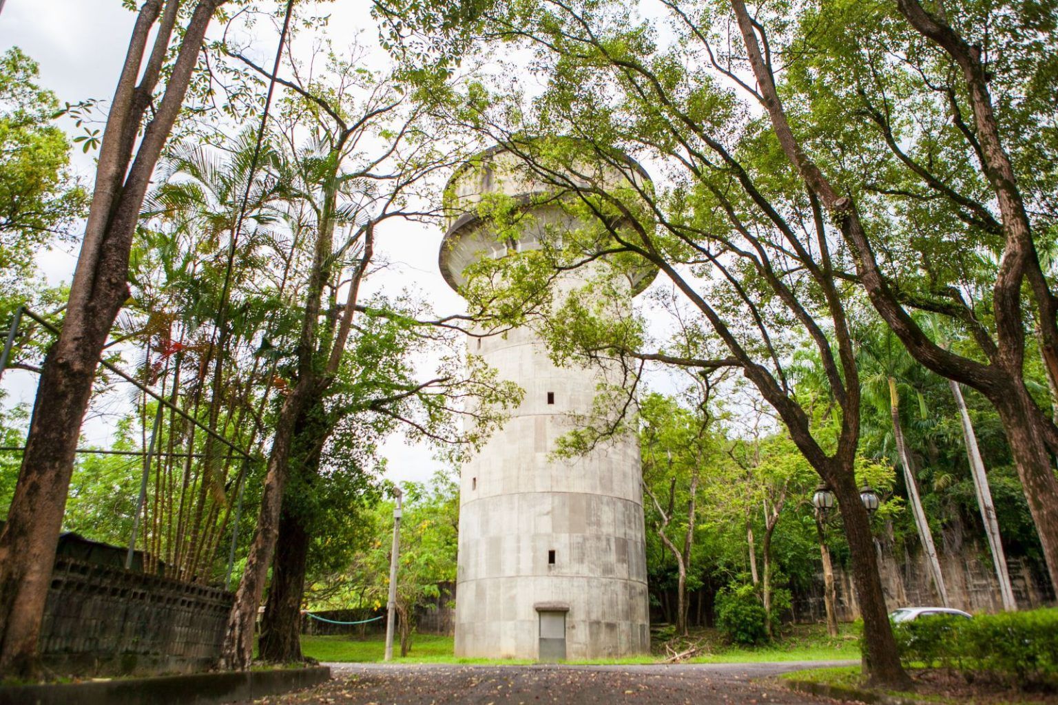 高聳的白色混凝土塔樓矗立在綠樹成蔭的公園中,周圍環繞著青草和陰雲密佈的天空。