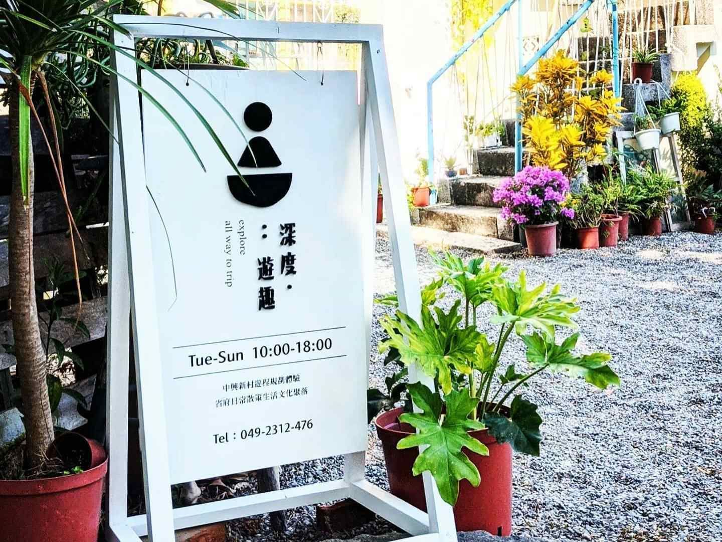 咖啡館外，白色招牌上用黑色字體寫著日文，旁邊是盆栽植物和碎石小路。