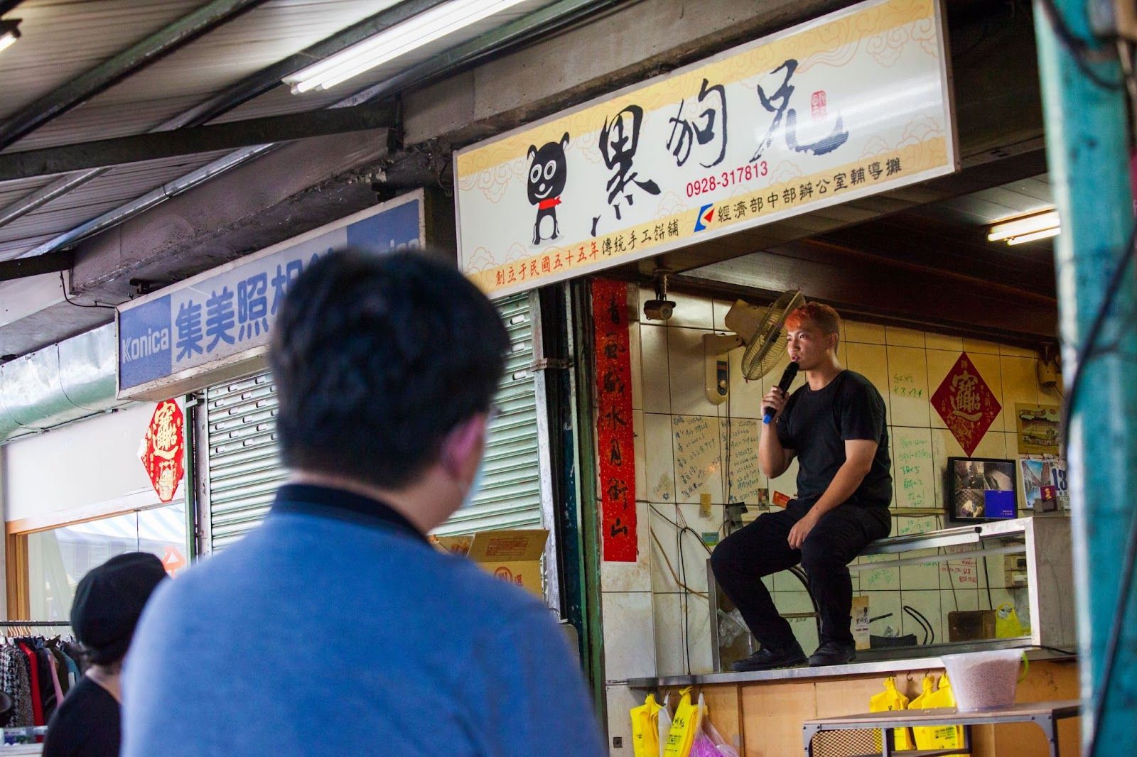 街頭藝人在店面外的小舞台上唱歌,前景中有個男人在看。