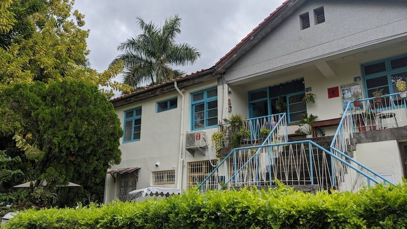 從下方拍攝的白色房屋,帶有藍色裝飾和前廊,周圍環繞著樹木和樹籬。