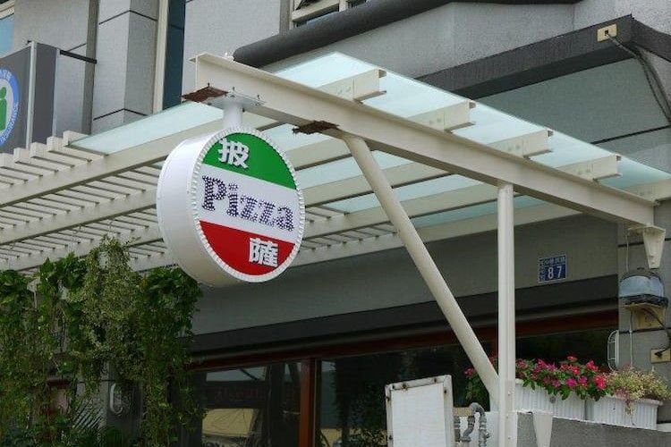圓形紅白相間的必勝客招牌懸掛在帶有白色遮陽篷的店面外。