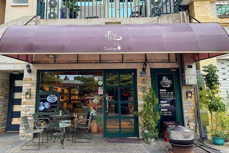 小型咖啡館店面，配有栗色遮陽篷、玻璃門、戶外桌椅和盆栽植物。