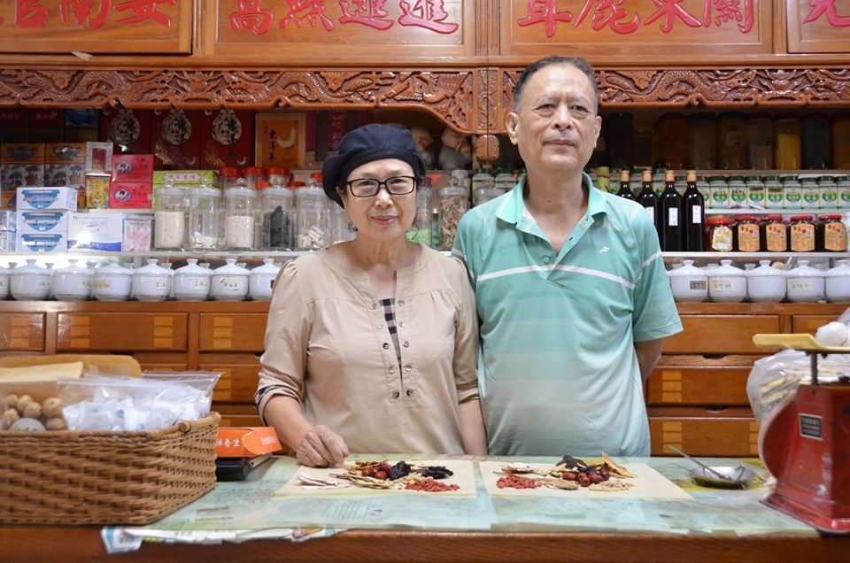 兩個人站在一家色彩繽紛的麵包店的櫃檯後面，櫃檯後面擺放著糕點和飲料。
