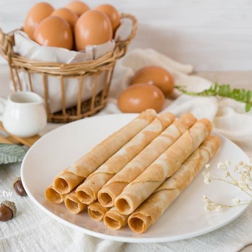 白色盤子上放著華夫餅卷，籃子裡裝著雞蛋，擺放在一張淺色鄉村風格的桌子上。