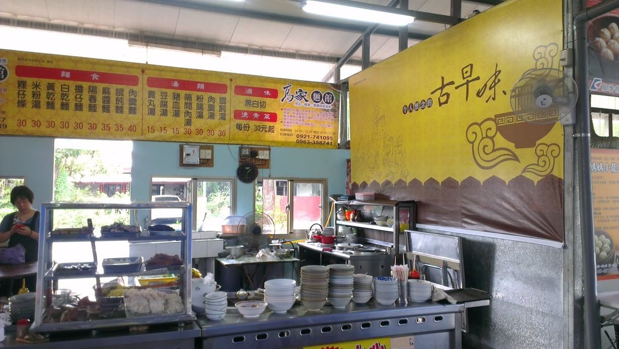 小型食品攤位內部，配有金屬櫃檯、懸掛式菜單牌和黃色牆飾。