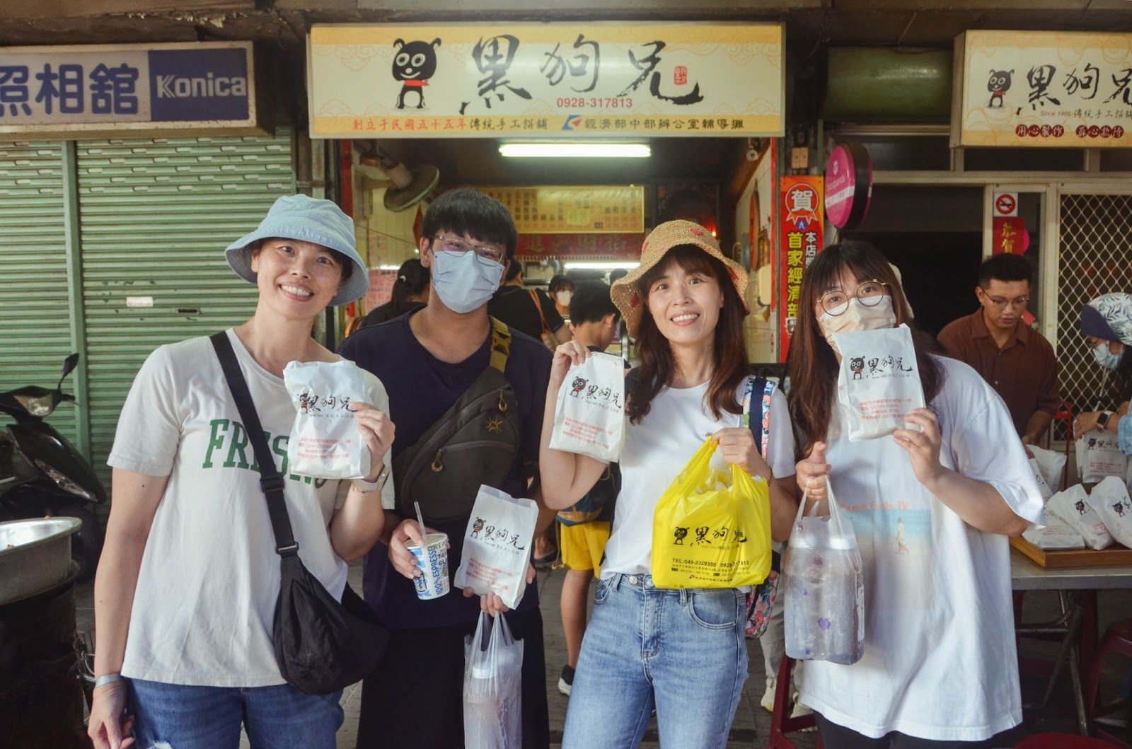 五個人戴著口罩,穿著休閒夏裝,在商店前拿著飲料擺姿勢拍照。