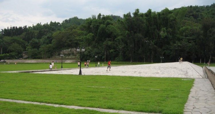 綠草茵茵的公園,鋪著白色石板路,幾個人在散步,遠處是樹木蔥的山坡。
